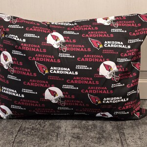 May include: Black pillow with a repeating pattern of the Arizona Cardinals logo, helmet, and text. The pillow is rectangular and has a soft, plush appearance, perfect for a sports fan.