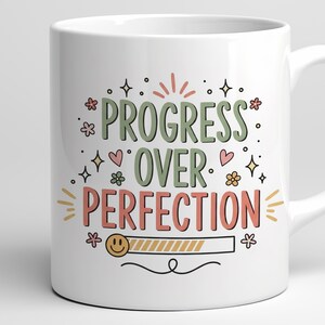 May include: White ceramic mug with the words "PROGRESS OVER PERFECTION" in green and coral lettering. The mug is decorated with small hearts, flowers, and stars. A smiling face and a progress bar are also featured.