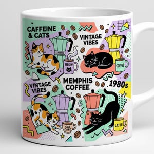 Op de afbeelding: Witte keramische mok met een kleurrijk Memphis-ontwerp met katten, koffiepotten, koffiebonen en de woorden "Caffeine & Cats", "Vintage Vibes", "Memphis Coffee" en "1980s". De mok heeft een handvat aan de rechterkant.