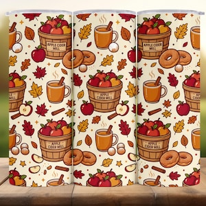 May include: A cylindrical tumbler featuring a repeating pattern of autumn-themed illustrations on a cream background. The design includes wooden baskets labeled Apple Cider Mill filled with red and yellow apples, mugs of cider, donuts, and leaves.