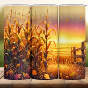 Puede incluir: Un vaso cilíndrico con un diseño otoñal. El diseño muestra un campo de maíz en tonos amarillos, naranjas y verdes, con hojas cayendo y una puesta de sol sobre un campo cosechado. El vaso tiene un acabado brillante.