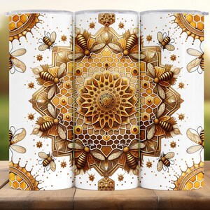 May include: Three white insulated tumblers featuring a repeating pattern of bees, honeycombs, and floral designs in gold and brown hues. The design is symmetrical, with a central mandala-style motif. The tumblers are cylindrical and have a glossy finish.
