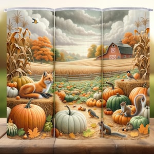 May include: A tumbler featuring a fall harvest scene. The design includes a red barn, pumpkins, a fox, and squirrels. The background shows a field with hay bales and a cloudy sky. The tumbler is cylindrical and made of stainless steel.