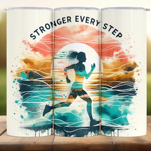 May include: A white tumbler with a watercolour design of a running figure against a sunset. The design includes the text "STRONGER EVERY STEP" in a curved font. The colour palette includes orange, teal, and brown.