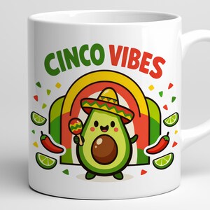 May include: White ceramic mug with the words "CINCO VIBES" in green and red. The mug features a cartoon avocado character wearing a sombrero and holding a maraca. The design includes a rainbow, chilli peppers, and lime slices.