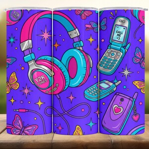 May include: A cylindrical tumbler featuring a vibrant purple background with a repeating pattern of pink and blue headphones labeled Y2K TUNES, flip phones with the text CALL ME <3, colorful butterflies, and small four-pointed stars.