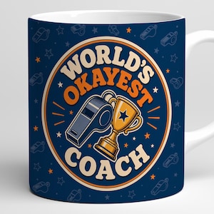 May include: A dark blue ceramic mug featuring a circular graphic with the text "WORLD'S OKAYEST COACH" in orange and cream. The design includes a gold trophy and a grey whistle, surrounded by a repeating pattern of small whistles and stars.