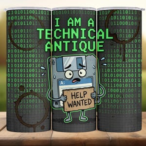 May include: A cylindrical tumbler with a humorous design. The tumbler features a cartoon floppy disk character holding a "Help Wanted" sign, with the text "I AM A TECHNICAL ANTIQUE" in green. Binary code and coffee stains decorate the background.