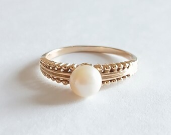 May include: A gold ring with a single white pearl set in the center. The band of the ring is decorated with a twisted rope design.