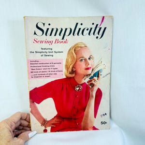 May include: A vintage Simplicity Sewing Book with a cover featuring a person in a red dress holding a sewing pattern. The text reads Simplicity Sewing Book featuring the Simplicity Unit System of Sewing, including details on garment construction, finishing, and charts.