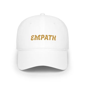 May include: A white baseball cap with the word "EMPATH" in a gold, cursive font across the front. The cap has a curved brim and a structured crown, suitable for casual wear.