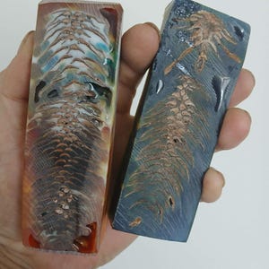 May include: Two resin blanks with a pine cone design. One blank is a mix of red, orange, and blue colours. The other blank is a mix of blue, green, and brown colours.