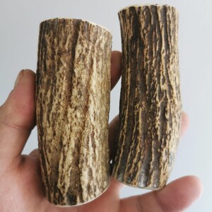 Peut inclure: Deux objets cylindriques à l'aspect texturé, semblable à de l'écorce. Les objets sont principalement bruns avec des accents beiges plus clairs et ont une esthétique rugueuse et naturelle. Les articles sont tenus dans une main, ce qui suggère qu'ils sont petits et portables.