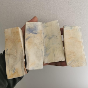 Peut inclure: Quatre blocs rectangulaires blanc cassé à la texture rugueuse, avec des marques bleues et marron. Les blocs sont tenus dans une main, mettant en valeur leur forme et leurs variations de couleur. Les blocs semblent être en bois.