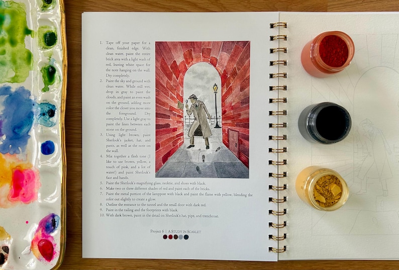 Puede incluir: Un cuaderno de bocetos abierto con encuadernaci&oacute;n en espiral, con una ilustraci&oacute;n en acuarela de Sherlock Holmes en un t&uacute;nel de ladrillos rojos. Se ven tres peque&ntilde;os botes de pintura y una paleta.