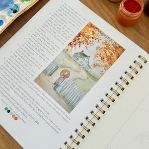 Puede incluir: Un libro de arte con espiral abierto en una acuarela de una casa con una valla blanca y follaje oto&ntilde;al. La p&aacute;gina incluye instrucciones y muestras de color. Se ven botes de pintura y una paleta.