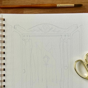 Puede incluir: Un cuaderno de espiral con un dibujo a l&aacute;piz de un armario. Un pincel y unas tijeras doradas est&aacute;n sobre la superficie de madera. El dibujo del armario tiene una parte superior decorativa con una cabeza de le&oacute;n y detalles florales.