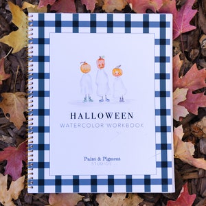 May include: A white watercolor workbook with a blue and white checkered cover. The cover features a title that reads "HALLOWEEN WATERCOLOR WORKBOOK" and a logo that reads "Paint & Pigment Studios". The cover also features an illustration of three pumpkins wearing ghost costumes.