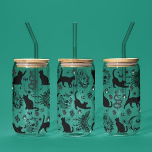 May include: Three glass tumblers with bamboo lids and glass straws. Each tumbler has a black cat and occult symbol pattern on a teal background. The design includes cats, skulls, and other mystical elements.