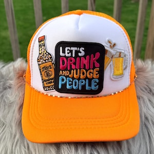 May include: Orange and white trucker hat with the text "LET'S DRINK AND JUDGE PEOPLE" on a black patch. The hat features a gold rope detail and patches of a vodka bottle and beer mugs.