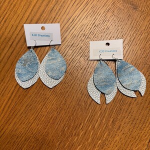 May include: Two pairs of teardrop-shaped earrings. The top layer is light blue denim, and the bottom layer is white with a textured, scale-like pattern. Each pair has a small white tag that reads "KJD Creations".