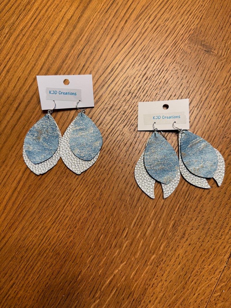 May include: Two pairs of teardrop-shaped earrings. The top layer is light blue denim, and the bottom layer is white with a textured, scale-like pattern. Each pair has a small white tag that reads "KJD Creations".