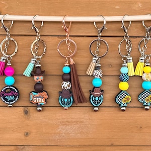 Portachiavi turchese con motivo western, ragazza di campagna, vanga, girasole, cappello da cowboy, borsa, zaino, sella, briglia e ciondolo con nappa in pelle.