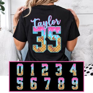 May include: Black t-shirt with the name "Taylor" in pink script above the number "35". The number is designed with a waffle pattern and dripping pink and blue frosting. A selection of numbers 0-9 is displayed below.