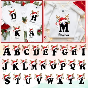 May include: White t-shirts and a sweatshirt featuring a Christmas-themed design. Each item displays a letter of the alphabet, a Santa hat, reindeer antlers, and a name. The letters are in black, with colorful ornaments.