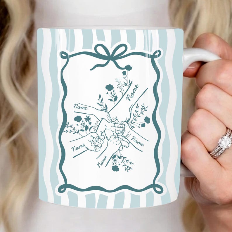 May include: White ceramic mug with a light blue and white striped background. The mug features a teal-coloured frame with a bow at the top, enclosing a design of hands holding each other, with the word "Name" written on each hand.