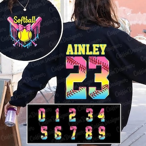 Può includere: Felpa nera con un design da softball sul davanti e sul retro. La parte anteriore presenta mazze incrociate, una palla da softball e la parola "Softball". Il retro mostra un nome e il numero 23 in un design da baseball. Vengono mostrati numeri aggiuntivi.