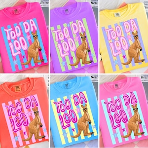 May include: A collection of six crew neck sweatshirts in various colors, each featuring a kangaroo wearing sunglasses and the text "TOO DA LOO" in a bubble font. The kangaroo is set against a striped background with stars.