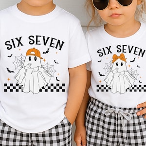 May include: White t-shirts with the text "SIX SEVEN" above a cartoon ghost wearing a hat or bow. The ghost is surrounded by bats, spiderwebs, and a checkered border. The shirts are for children.