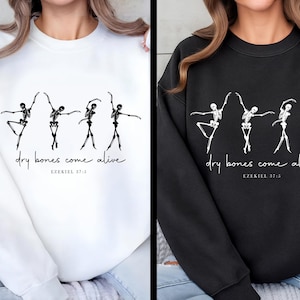 May include: White and black sweatshirts featuring a skeletal ballet dancer design. The phrase "dry bones come alive" and the Bible verse Ezekiel 37:5 are printed below the dancers. The sweatshirts are a comfortable, casual style.