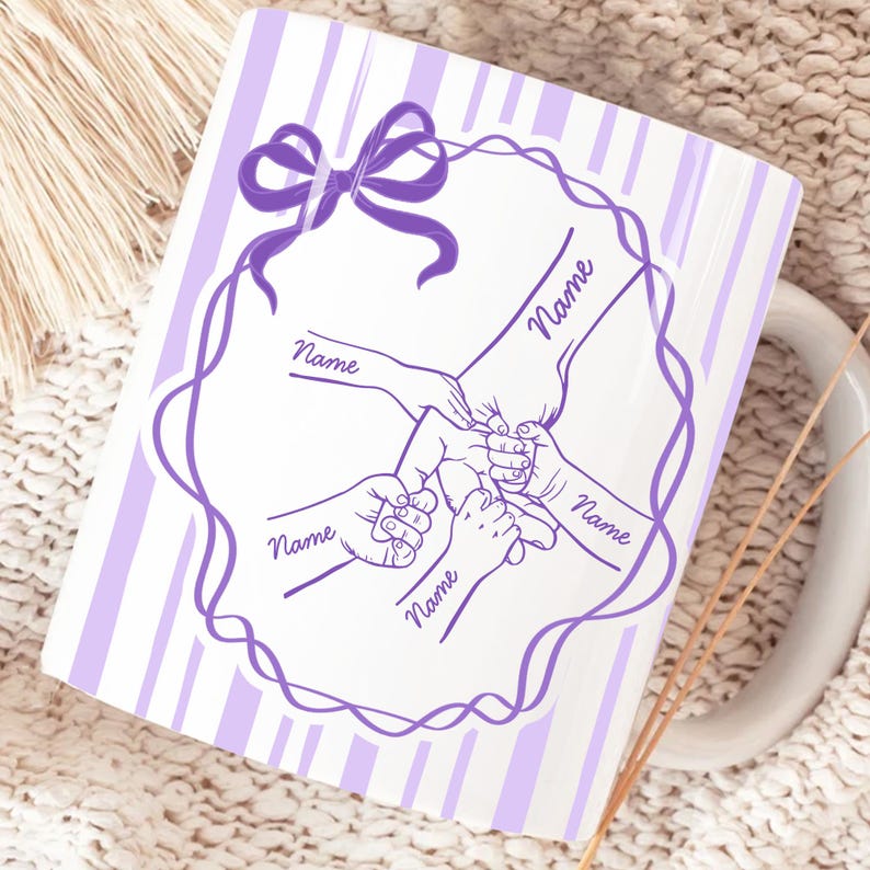 May include: White ceramic mug with a purple bow and a design of hands holding each other. The mug has a purple striped background and the word "Name" is written on the design.
