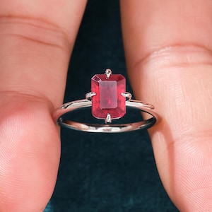 May include: A silver ring with a red emerald-cut gemstone.