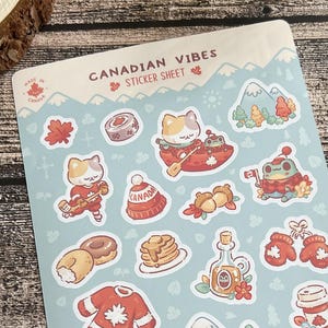 May include: A sticker sheet featuring Canadian-themed illustrations, such as a cat, maple leaves, and mountains. The sheet is light blue and has the text "CANADIAN VIBES STICKER SHEET". Two pens with heart and scenic designs are also visible.