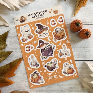 May include: A sheet of Halloween Kitties stickers on an orange background. The stickers feature various cats in witch hats, pumpkins, and potion bottles. The text "Halloween Kitties + Sticker Sheet" is at the top. Two small pumpkins are next to the sticker sheet.