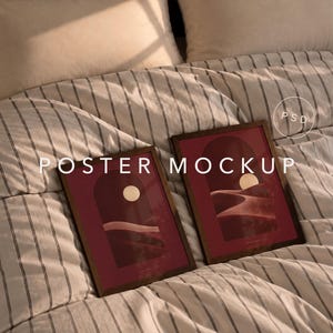 May include: Two rectangular wooden frames containing posters with a dark red background, an arched doorway graphic, and a circular sun shape above rolling hills. The text "POSTER MOCKUP" and a circular "PSD" icon are overlaid on the image.