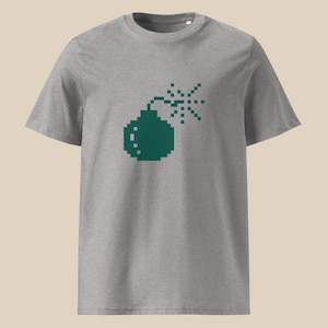 May include: A gray t-shirt featuring a pixelated green bomb graphic. The design includes a round bomb shape with a lit fuse and an explosion effect. The shirt has short sleeves and a crew neck.