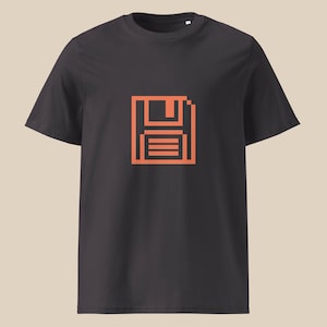 May include: Dark gray t-shirt featuring a pixelated orange floppy disk graphic. The short-sleeved tee has a crew neck and a simple, modern design. The graphic is centered on the chest, offering a retro tech aesthetic.