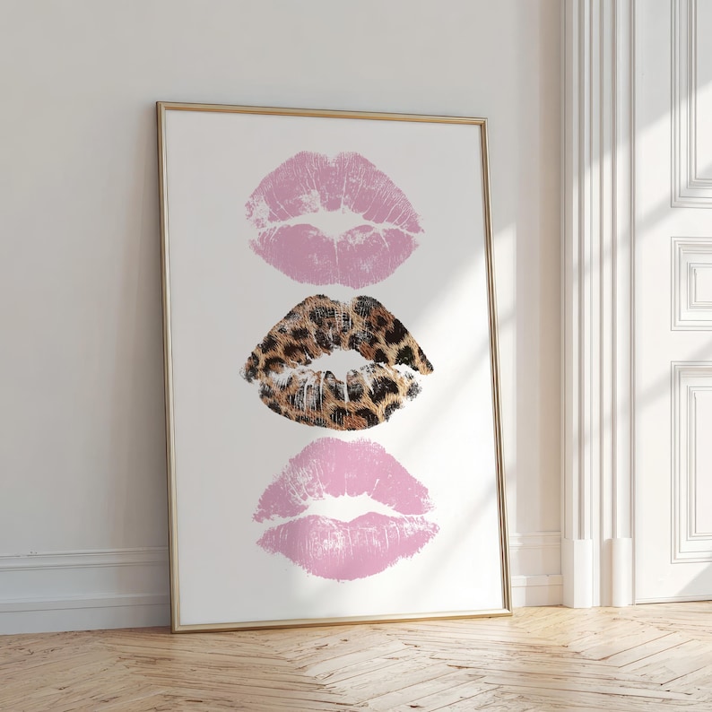 May include: A framed print featuring three lip prints. The top and bottom prints are a soft pink, while the middle print has a leopard print design. The artwork is displayed on a white background.