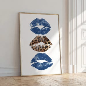 Puede incluir: Impresión enmarcada con tres huellas de labios. Las huellas superior e inferior son de color azul oscuro, mientras que la del medio tiene un estampado de leopardo. La obra de arte se muestra sobre un fondo blanco.