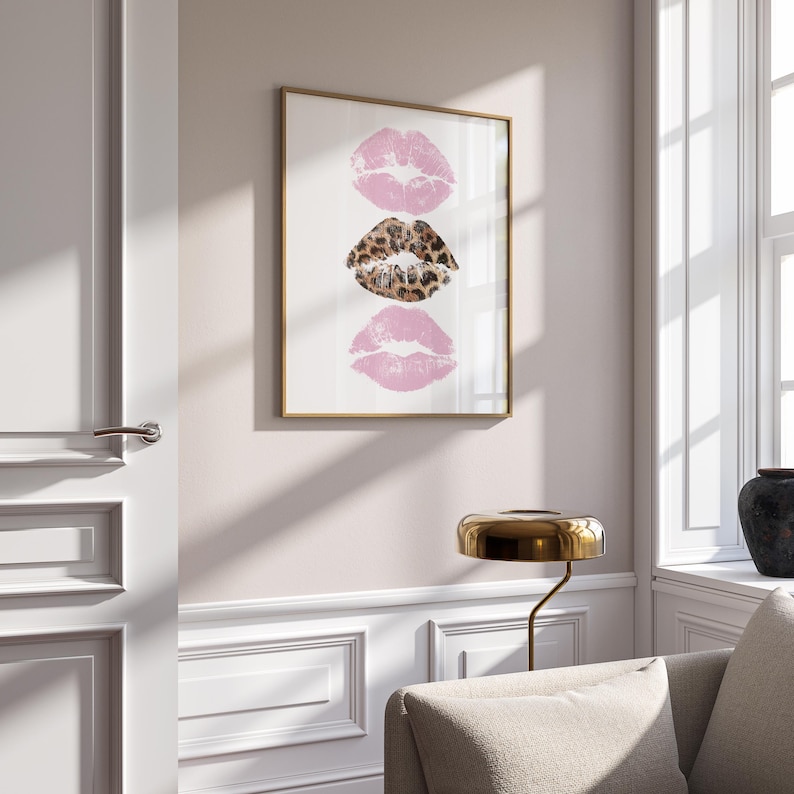 May include: Framed art print featuring three lip prints. Two pink lip prints flank a central leopard print lip print. The artwork is displayed in a gold frame against a white background, adding a touch of glamour to any space.