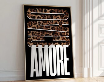 May include: A framed art print with the word "DAD" in a leopard print pattern, and the word "AMORE" in white block letters, set against a black background. The artwork is in a gold frame and leans against a white wall.