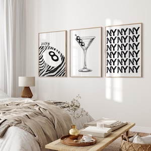 May include: Three black and white wall art prints.  The leftmost print features a zebra-striped eight ball with the word 'lucky' above it. The center print shows a martini glass with olives. The rightmost print is a repeating pattern of the letters 'NYNYNY'. These prints would add a stylish, modern touch to any room.