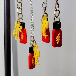 May include: Three silver chains with red and yellow bottle charms. The charms have the words "R.I.P.L", "H.Y.L", and "P.N.L" on them. The charms are attached to a key chain, necklace, and earrings.