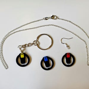 Peut inclure: Un collier en chaîne argentée, un porte-clés avec un charme rond noir avec un accent jaune, bleu ou rouge, et une paire de boucles d'oreilles avec des charmes ronds noirs avec un accent rouge ou bleu.