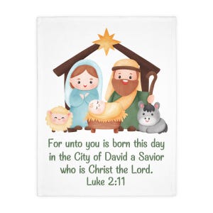 May include: A white blanket featuring a colourful cartoon nativity scene with Mary, Joseph, baby Jesus in a manger, a sheep, and a donkey under a star. The text reads: For unto you is born this day in the City of David a Savior who is Christ the Lord. Luke 2:11.