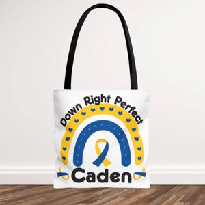 May include: White tote bag with black handles featuring a blue and yellow rainbow design and the text "Down Right Perfect Caden". The design includes a yellow ribbon and blue hearts.